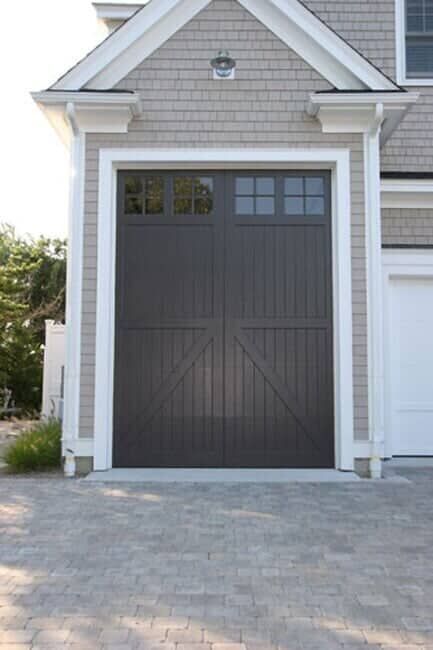 A tall, dark brown garage door with a carriage-style design and upper windows on a shingled house exterior.