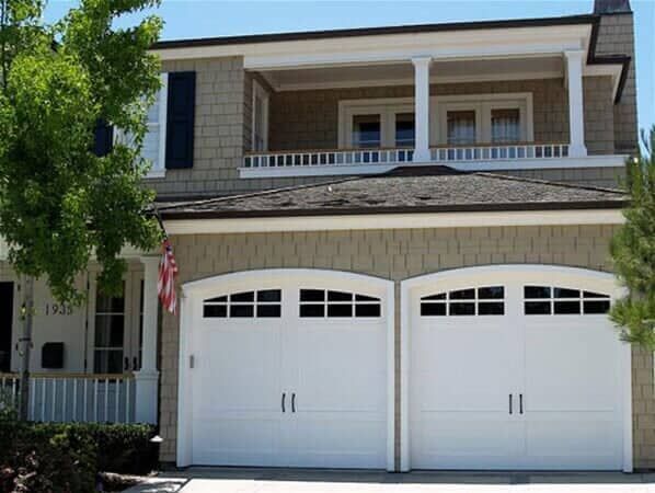 A two-story tan house with white trim, two white arched garage doors with windows, and a covered upper balcony.