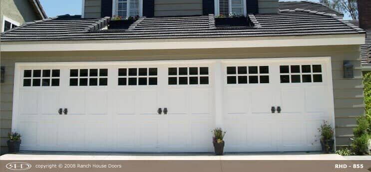 White three-car garage door with grid-style top windows and decorative black handles, installed on a house exterior.