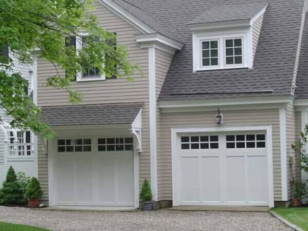 A light-colored two-story house with two white garage doors and a dormer window above the right garage.