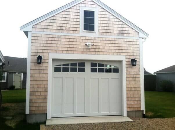 A detached garage with light-colored cedar shingle siding and a white, windowed carriage-style door.