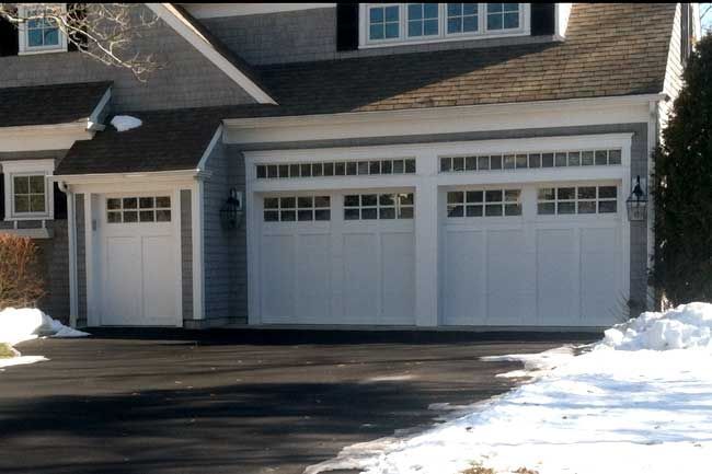 A modern house exterior featuring a white single-car garage door and a double-car garage door with window panels.