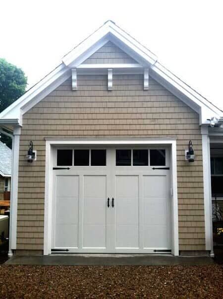 A tan, shingled garage with a white, carriage-style door and black decorative hardware, viewed from the exterior.