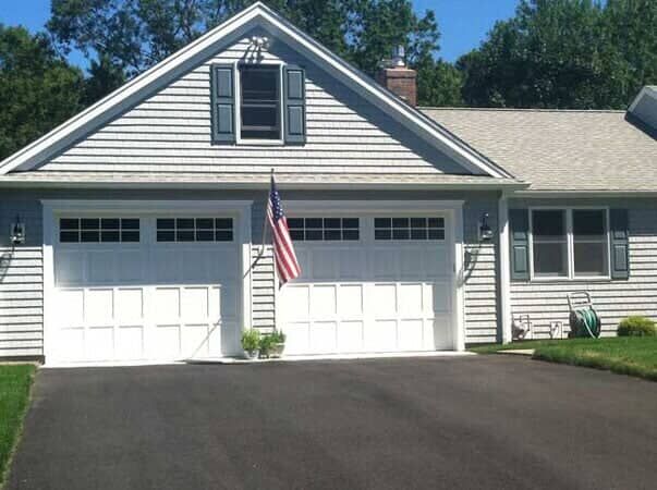 A house exterior with two white garage doors, grey siding, and an American flag displayed between them.