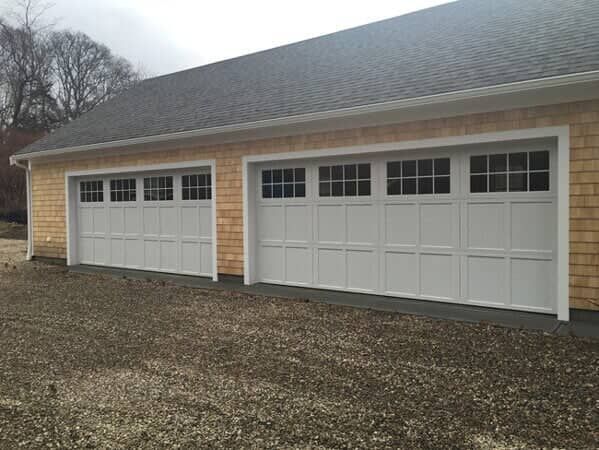 A light-colored building with two white carriage-style garage doors featuring rectangular windows.