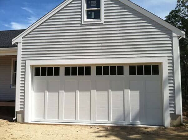 White carriage-style garage door with windows, set in a light grey vinyl-sided building exterior.