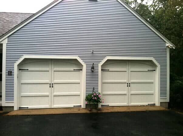 A blue-sided garage with two white, carriage-style doors and a potted plant centered between them.