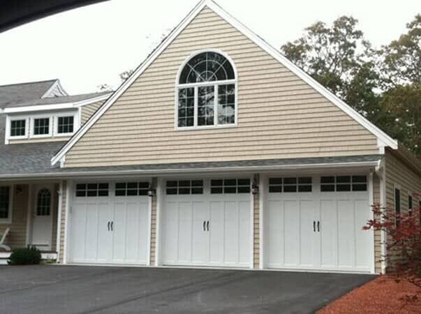 A large, tan house exterior featuring three white garage doors and an arched window above on the second level.