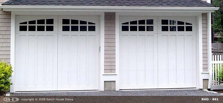 Two white garage doors with arched windows set in a house with light-colored siding.