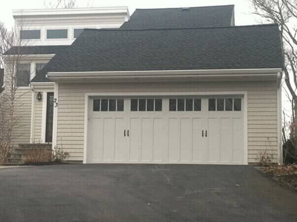 A suburban home exterior featuring light beige siding, a dark shingled roof, and a large white multi-pane garage door.