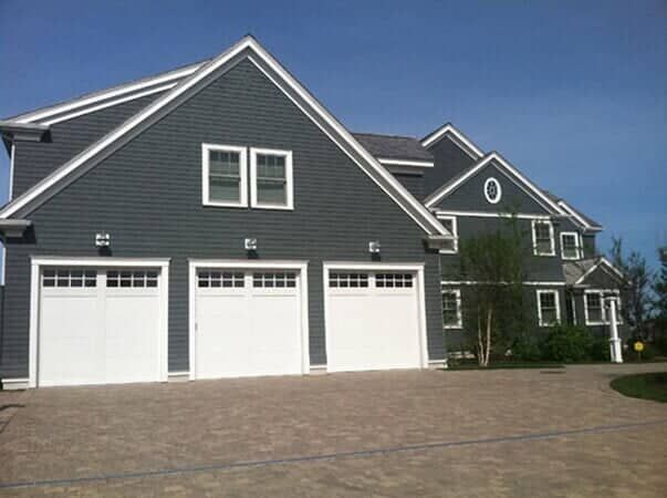 A large, dark blue house with three white garage doors and a paved driveway under a clear blue sky.