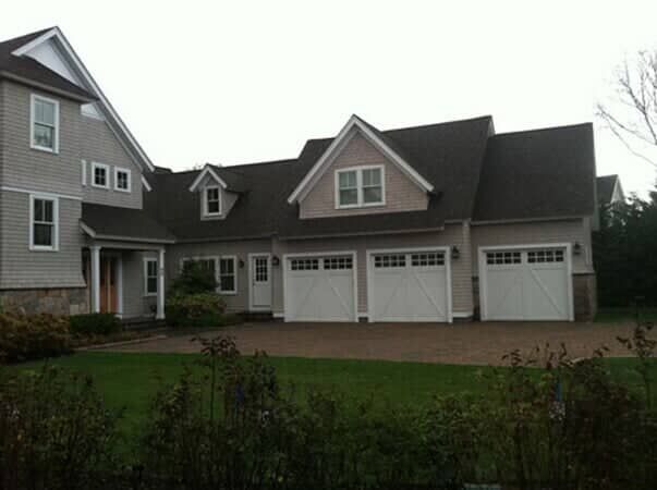 A large grey house with a three-car garage and a grassy front lawn.