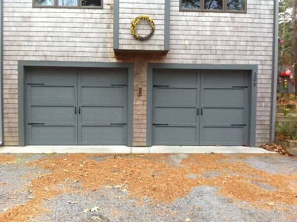 Two gray carriage-style garage doors on a cedar shingle house exterior, with a decorative wreath on the wall above.