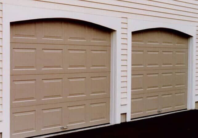 Two beige, arched-top garage doors set into a building with white siding.