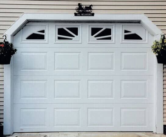White garage door with sunburst-style window panels, arched top frame, and hanging flower baskets on either side.