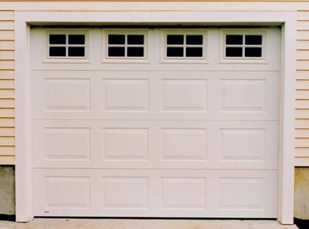 A white, four-panel residential garage door featuring a row of four small windows at the top.