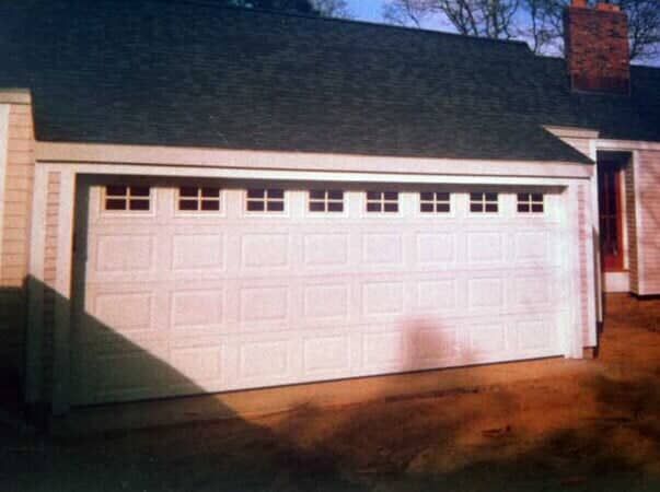 A white, multi-paneled garage door with a row of rectangular windows near the top, installed in a home exterior.
