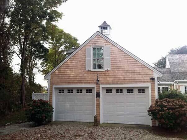A two-car garage with cedar shingle siding, a white window with shutters, and a cupola on the peaked roof.