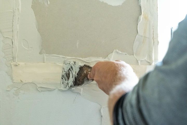 Person applying plaster to a damaged wall with a putty knife