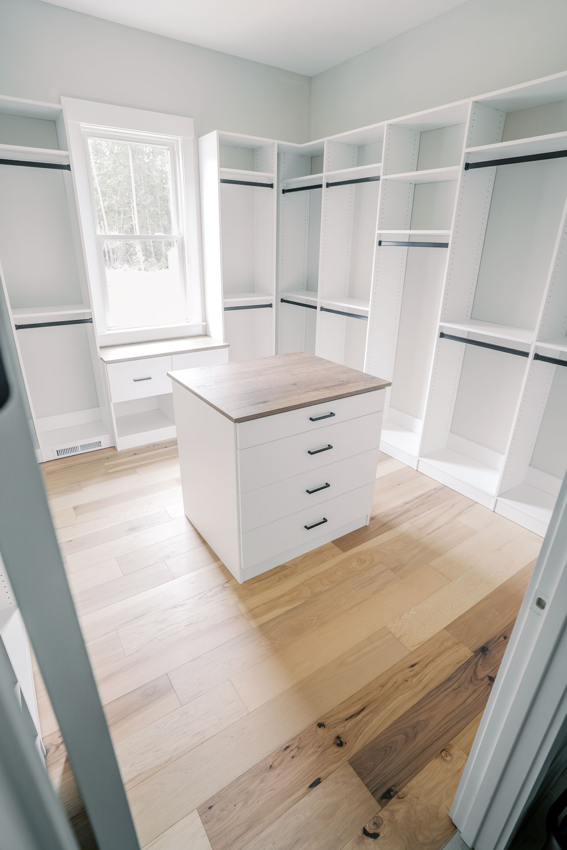 A walk in closet with wooden floors and white shelves.