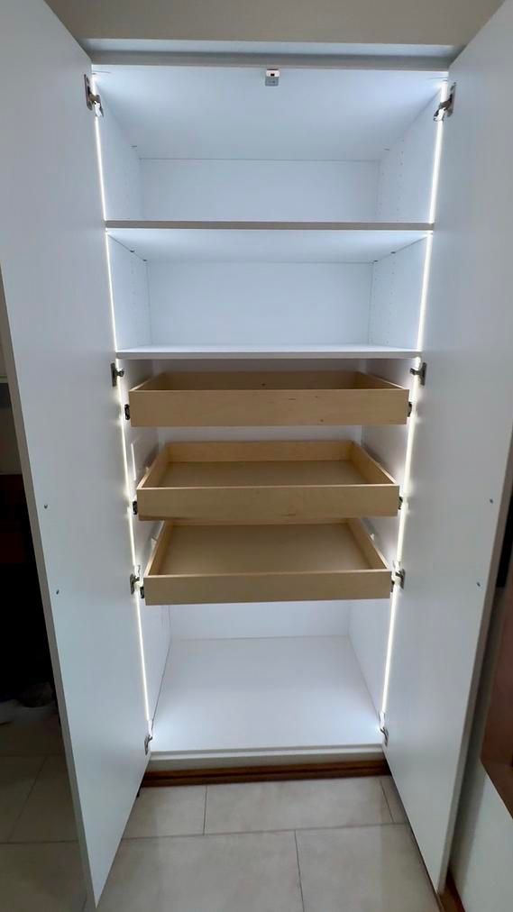 A white closet with wooden shelves and drawers and lights.