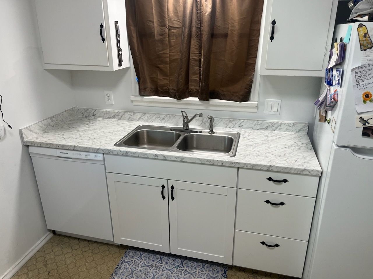 A kitchen with white cabinets , a sink , a refrigerator and a window.