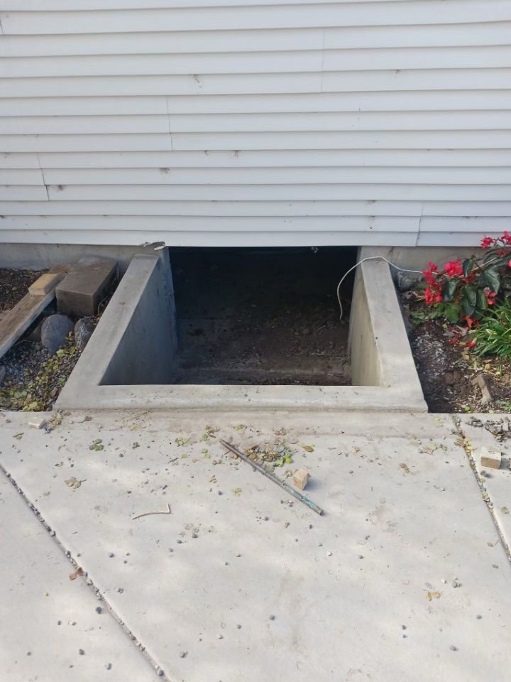 A concrete window well is being built into the side of a house.