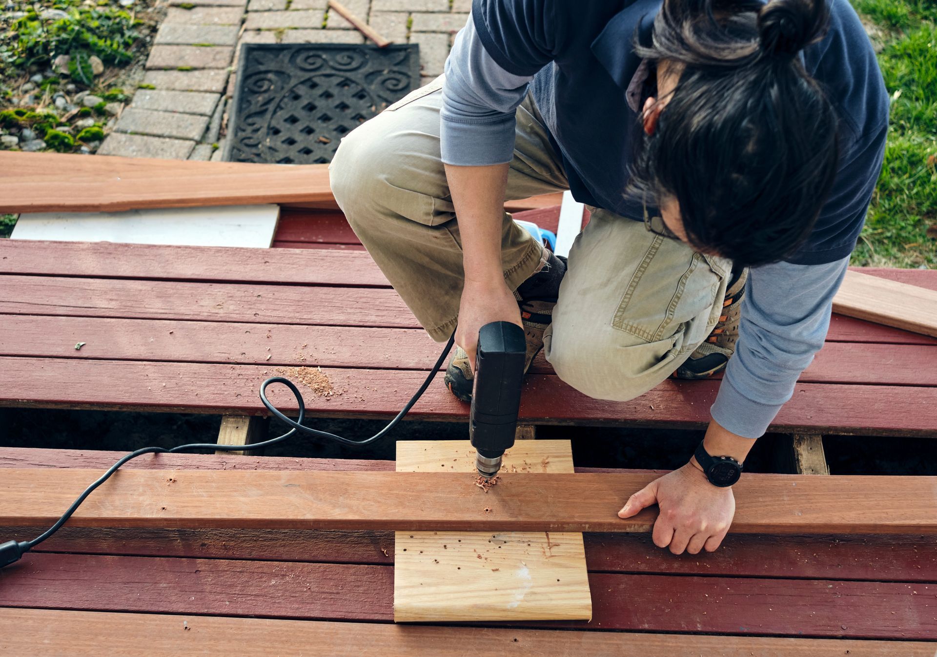 A woman is using a drill to drill a hole in a piece of wood.