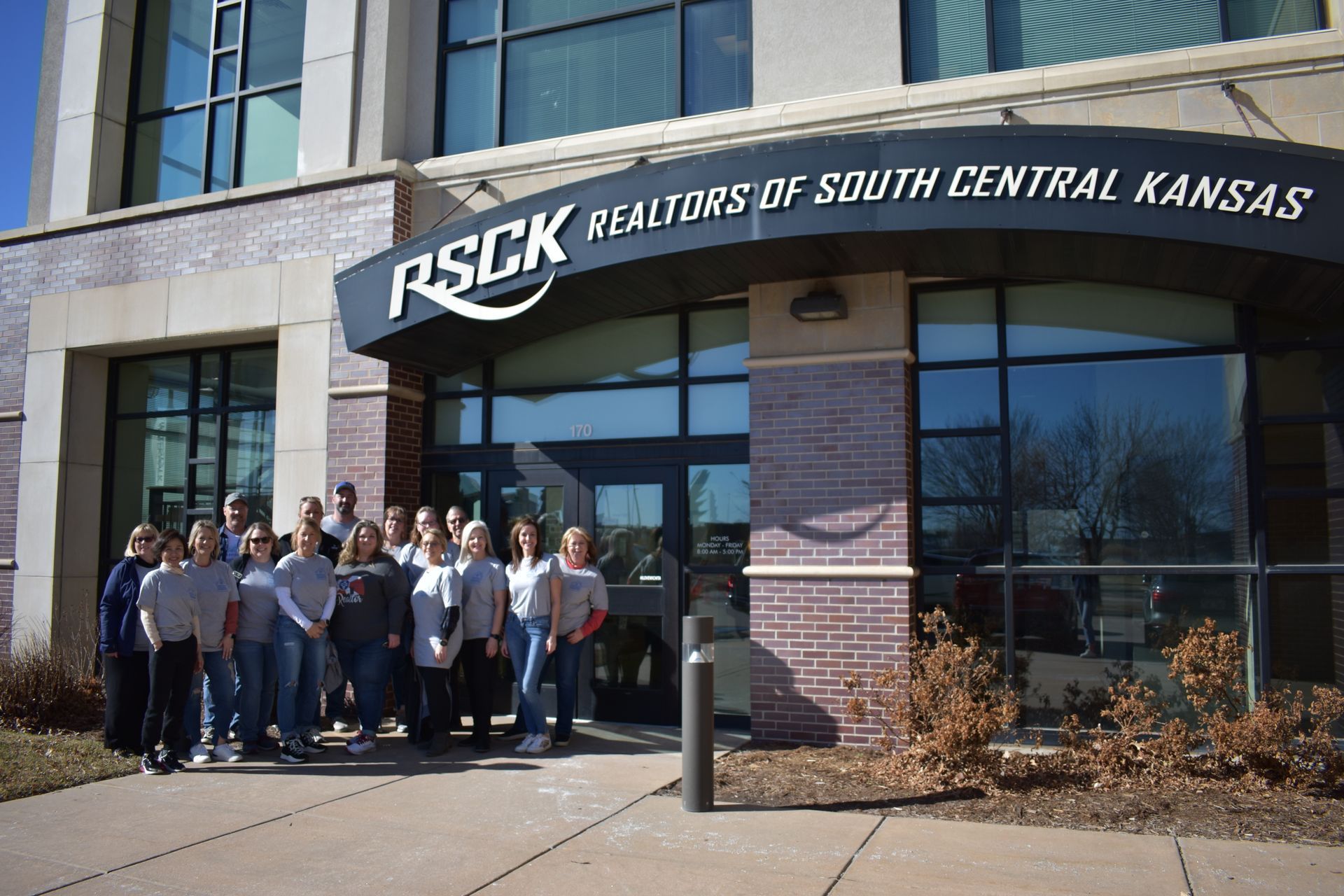 A group of people standing outside the entrance of the Realtors of South Central Kansas building.