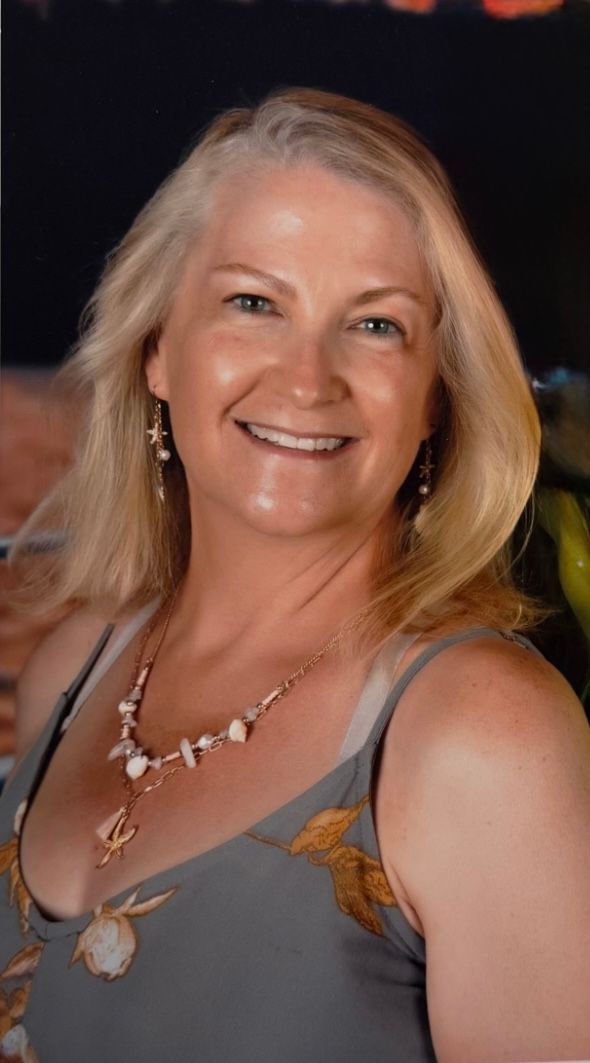 A person with long brown hair smiling at the camera, wearing a red top against a neutral background.