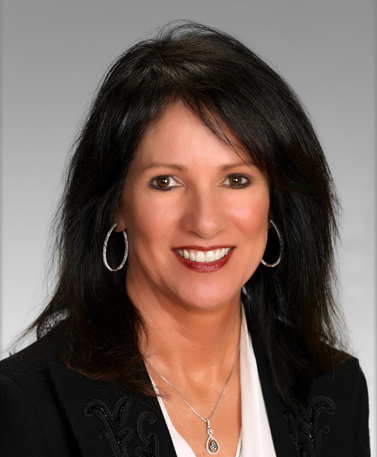 Headshot of a person with shoulder-length dark hair, wearing a black blazer, white shirt, and silver hoop earrings.