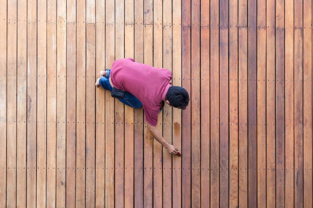 A Man Is Painting A Wooden Deck With A Brush — L & S Wirth Painting in Wellington, NSW