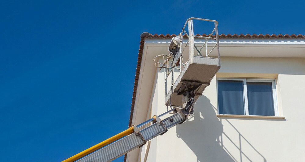 A Man Is Painting The Side Of A Building With A Crane — L & S Wirth Painting in Gilgandra, NSW