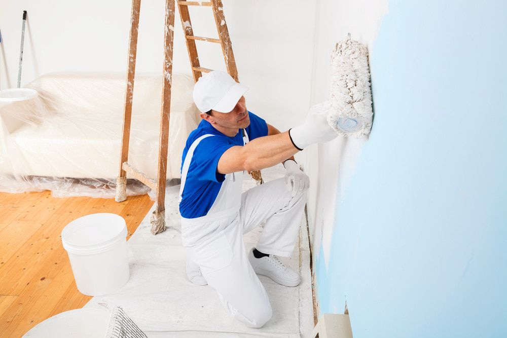 A Man Is Kneeling Down While Painting A Wall With A Paint Roller — L & S Wirth Painting in Coonamble, NSW