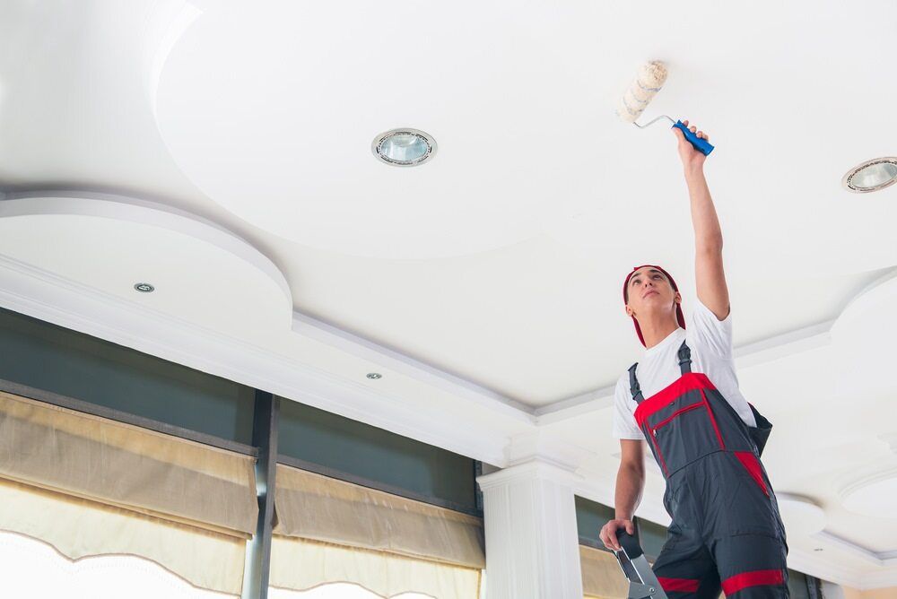 A Man Is Painting The Ceiling Of A Room With A Paint Roller — L & S Wirth Painting in Forbes, NSW