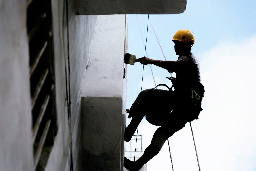 A Man In A Yellow Hard Hat Is Painting A Building — L & S Wirth Painting in Gilgandra, NSW