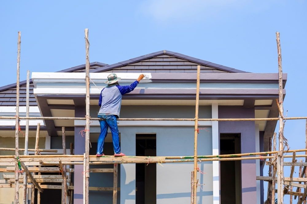 A Man Is Painting The Side Of A House On A Scaffolding — L & S Wirth Painting in Wellington, NSW