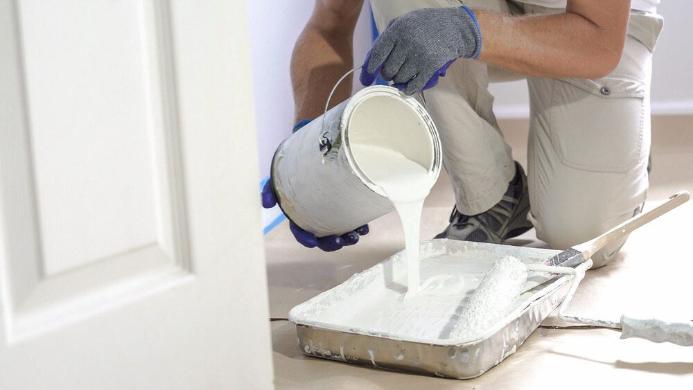 A Man Is Pouring White Paint Into A Paint Tray — L & S Wirth Painting in Dubbo, NSW