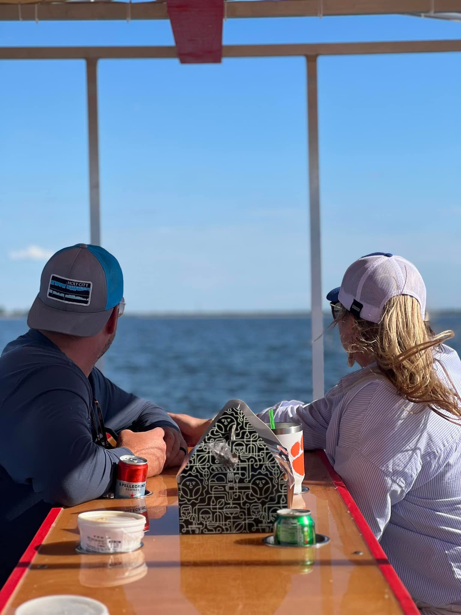 A man and a woman are sitting at a table on a boat looking at the ocean.