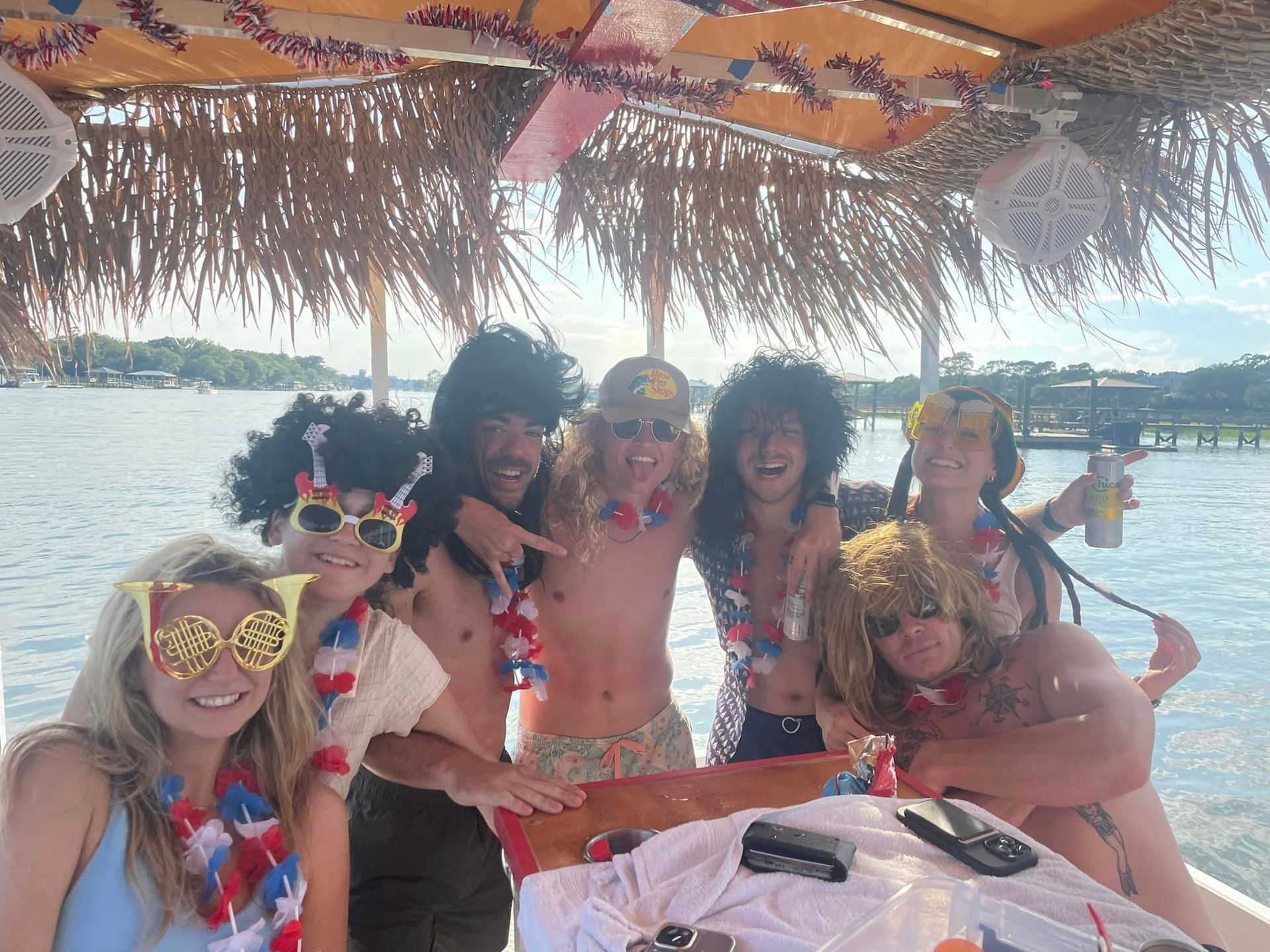 Group of people wearing colorful leis and sunglasses, posing under a thatched beach canopy on a boat.