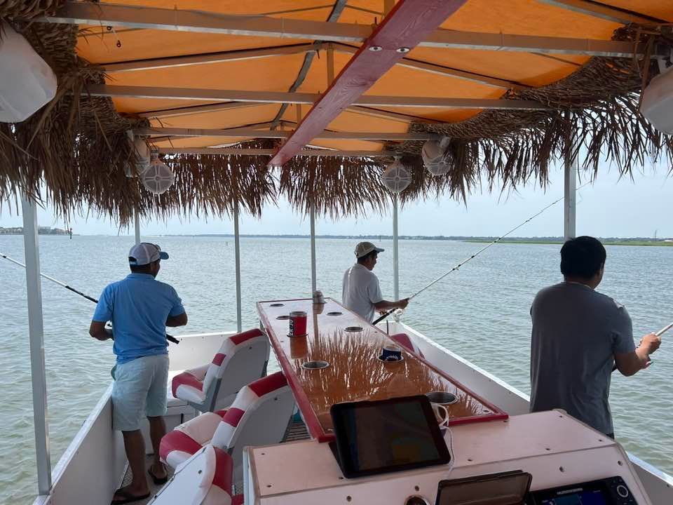 Three people fishing from a small boat with a thatched canopy on calm open water