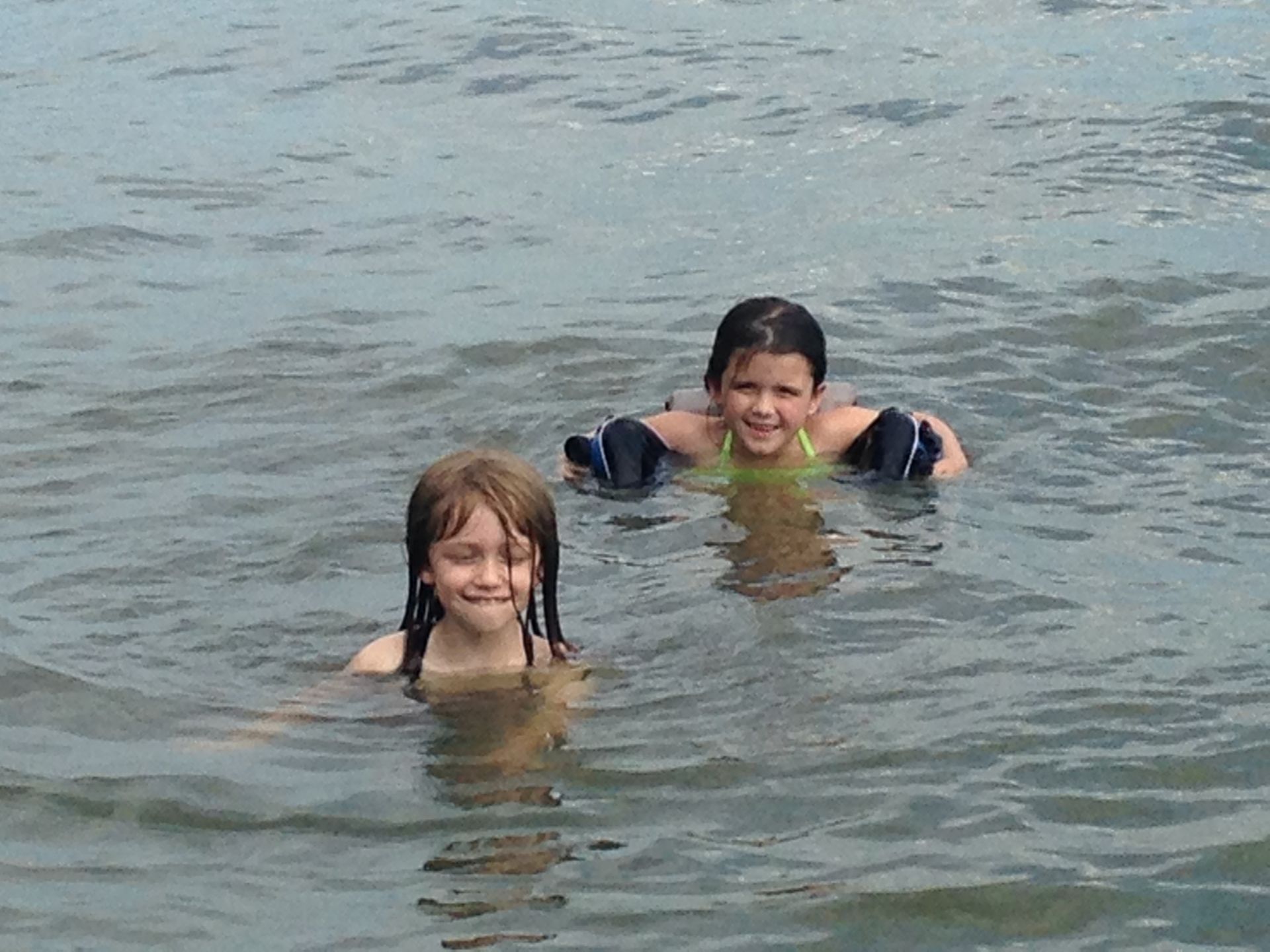 Two young girls are swimming in a body of water