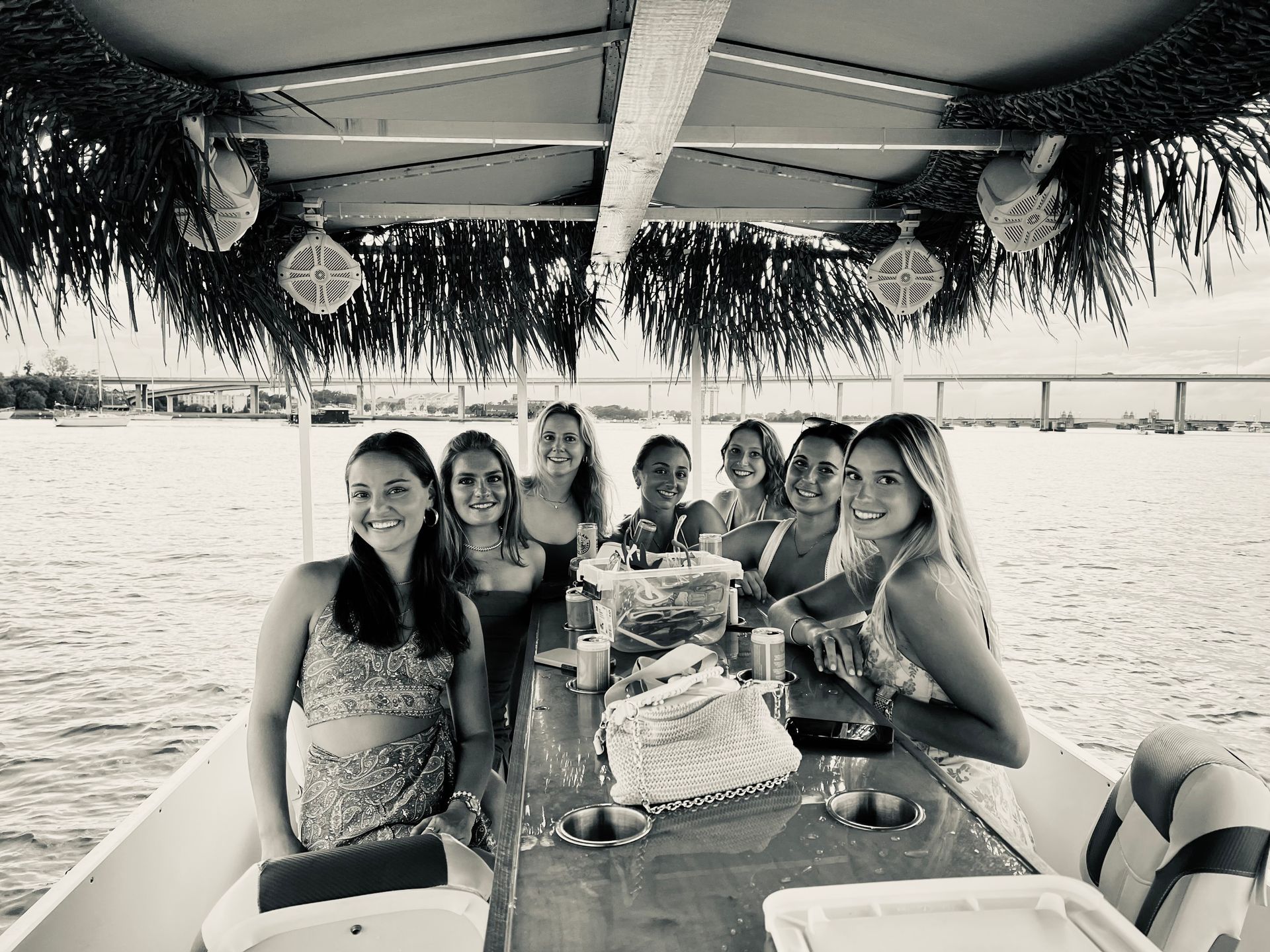 Group of friends seated at a table on a boat, smiling under a shaded canopy on the water.