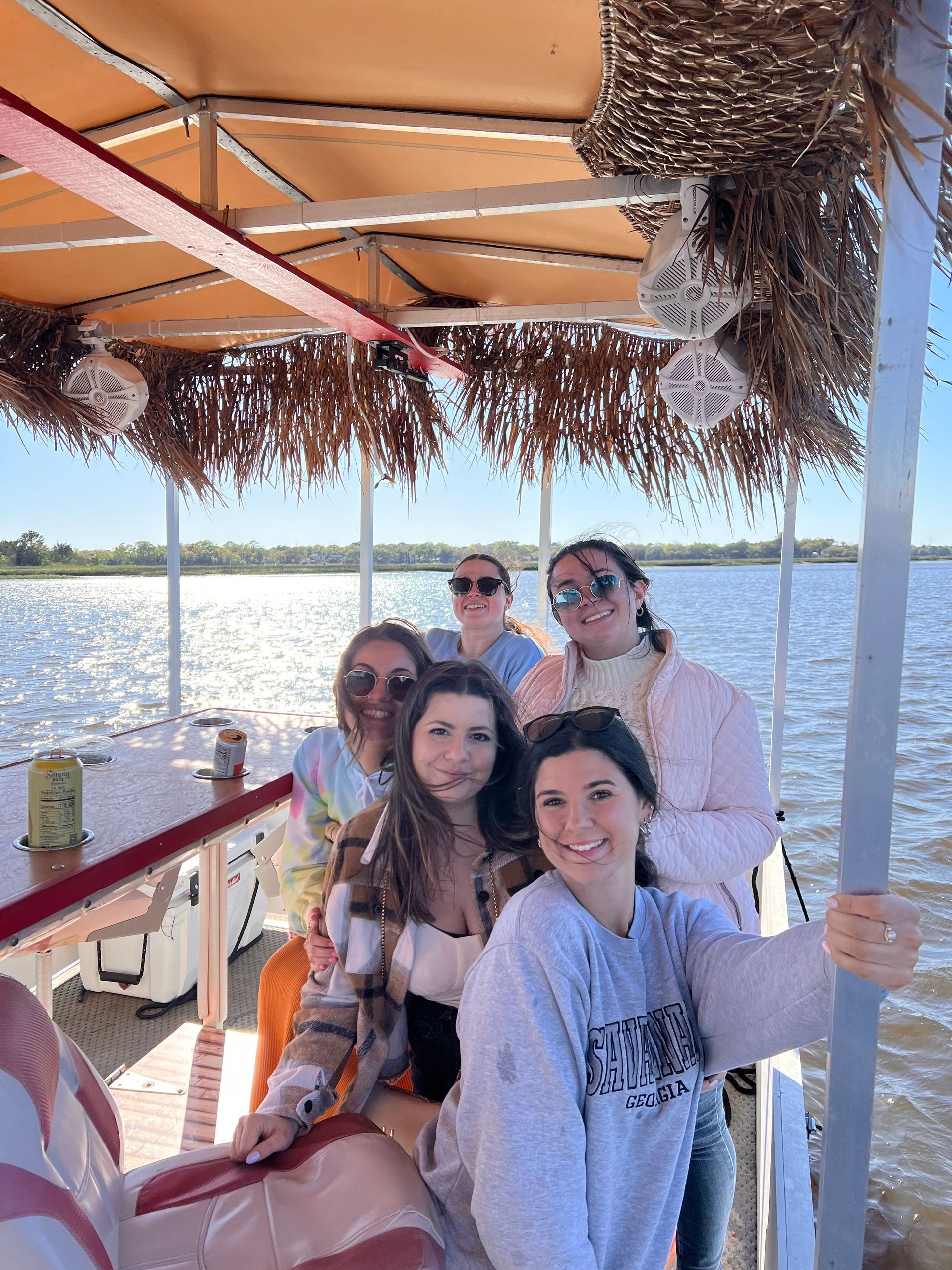 Five friends smiling on a boat with a thatched canopy and sparkling water behind them