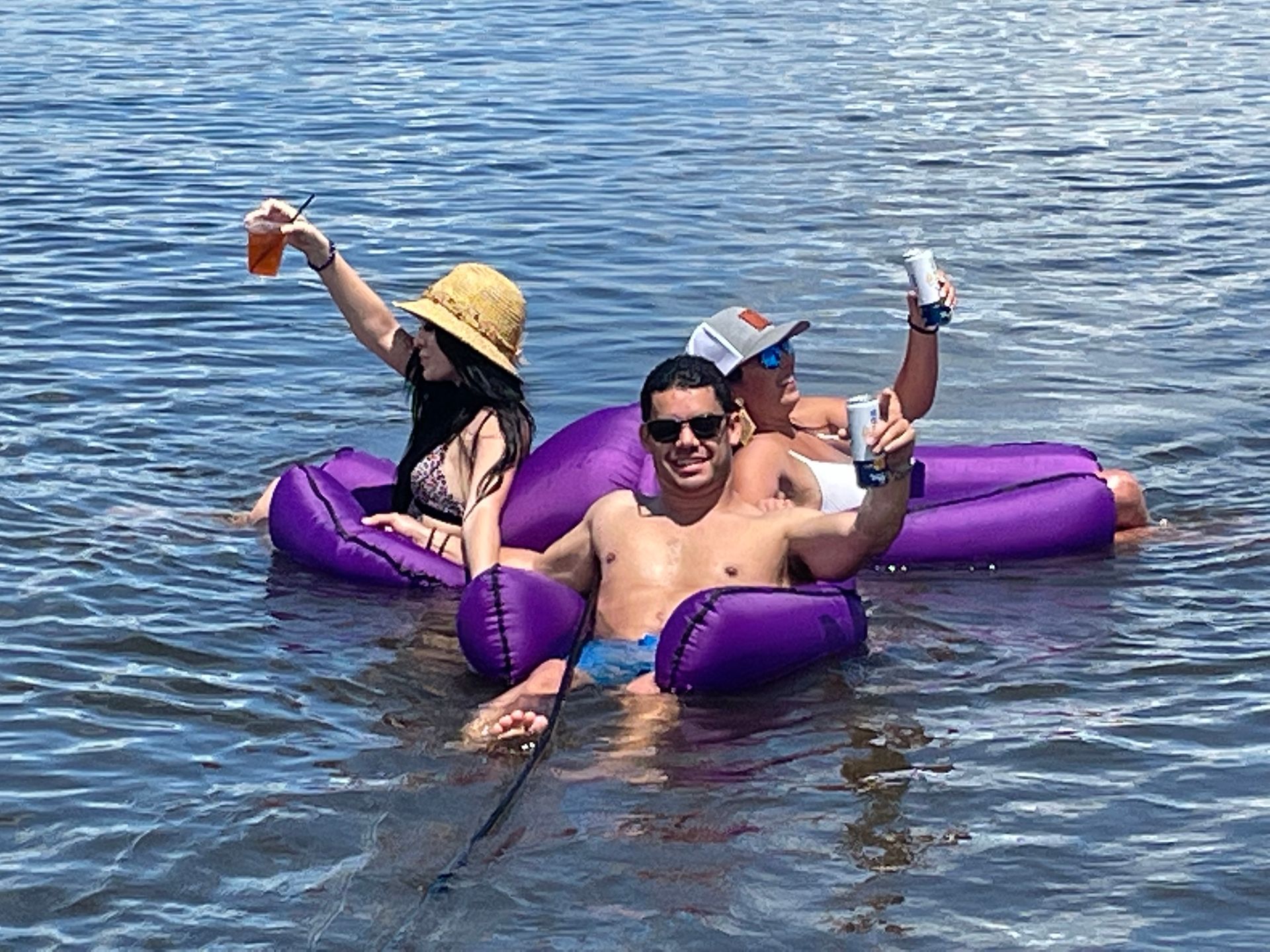 A man and a woman are floating on purple rafts in the water.