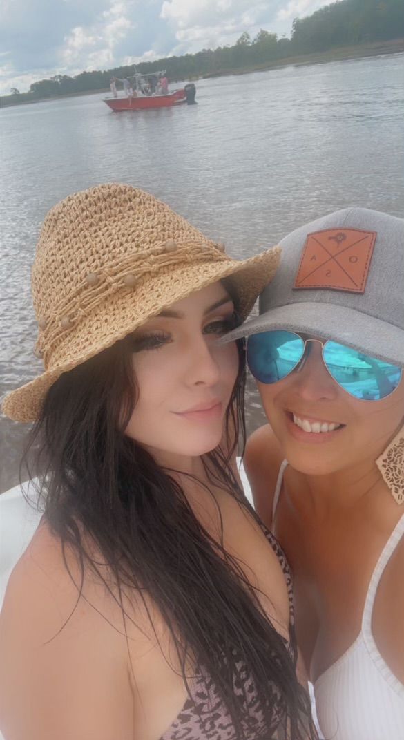 Two women wearing hats and sunglasses are standing next to each other on a boat.