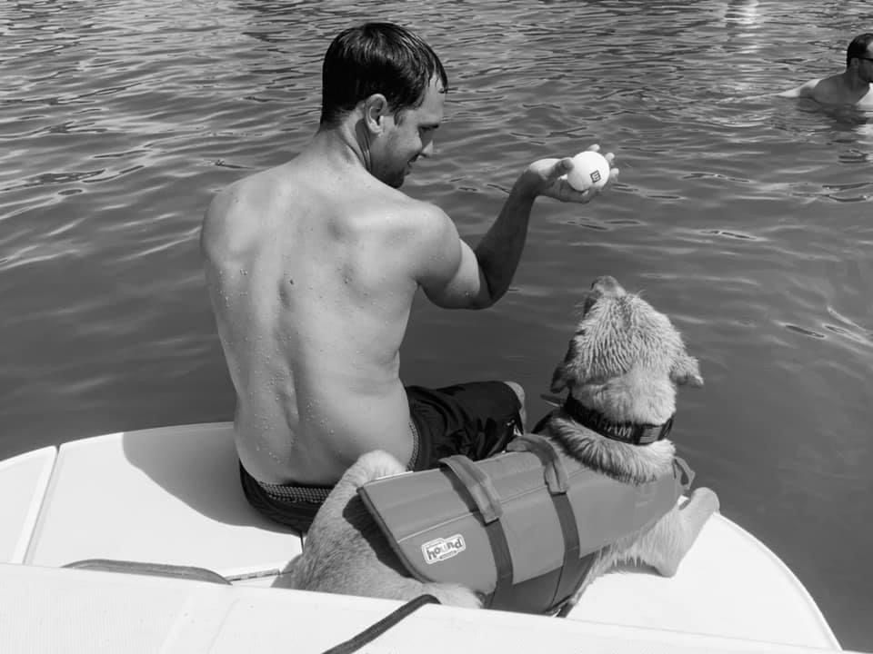 A man is sitting on a boat with a dog wearing a life jacket.