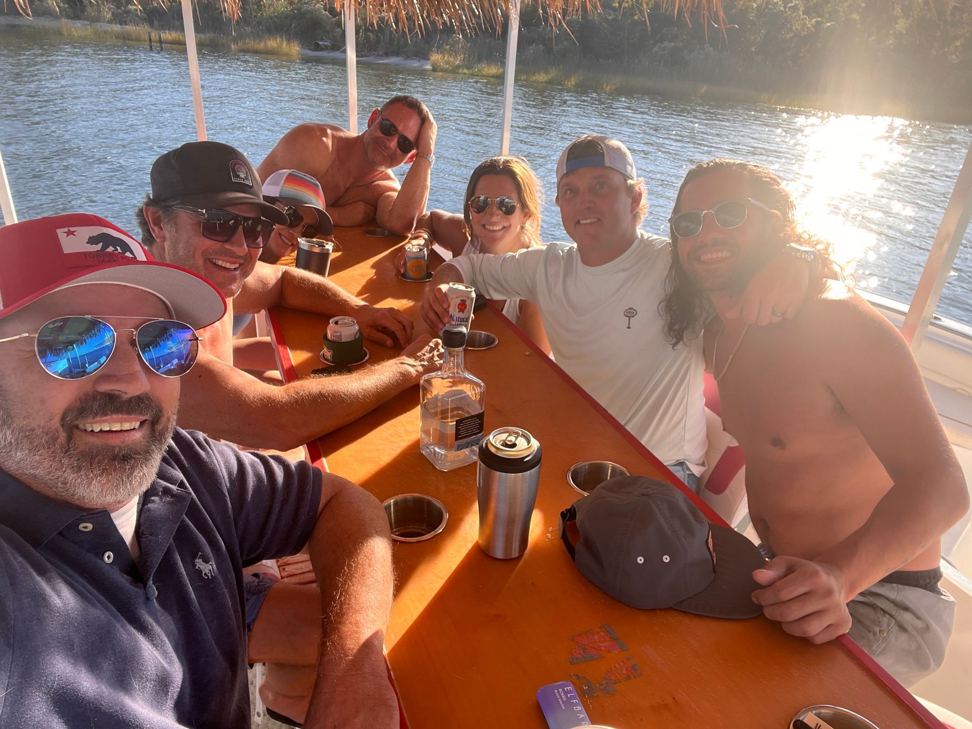 Group of friends smiling at an orange table on a boat in warm sunset light by the water