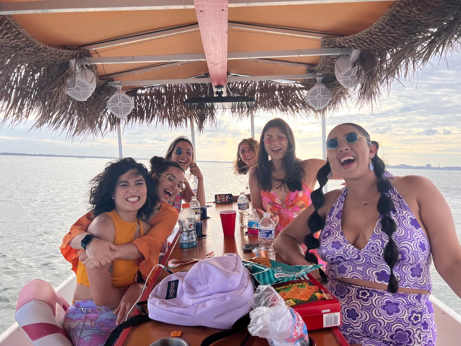 Group seated on a boat deck, smiling and holding drinks during a sunny waterfront outing.