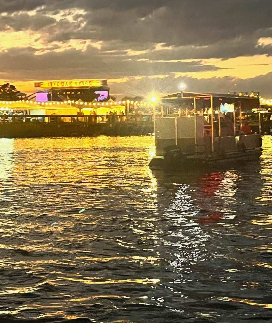 Boat on rippling water at sunset, with glowing lights and a lit waterfront skyline in the background